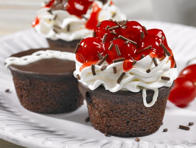 Three chocolate cupcakes with whipped cream and cherries on top