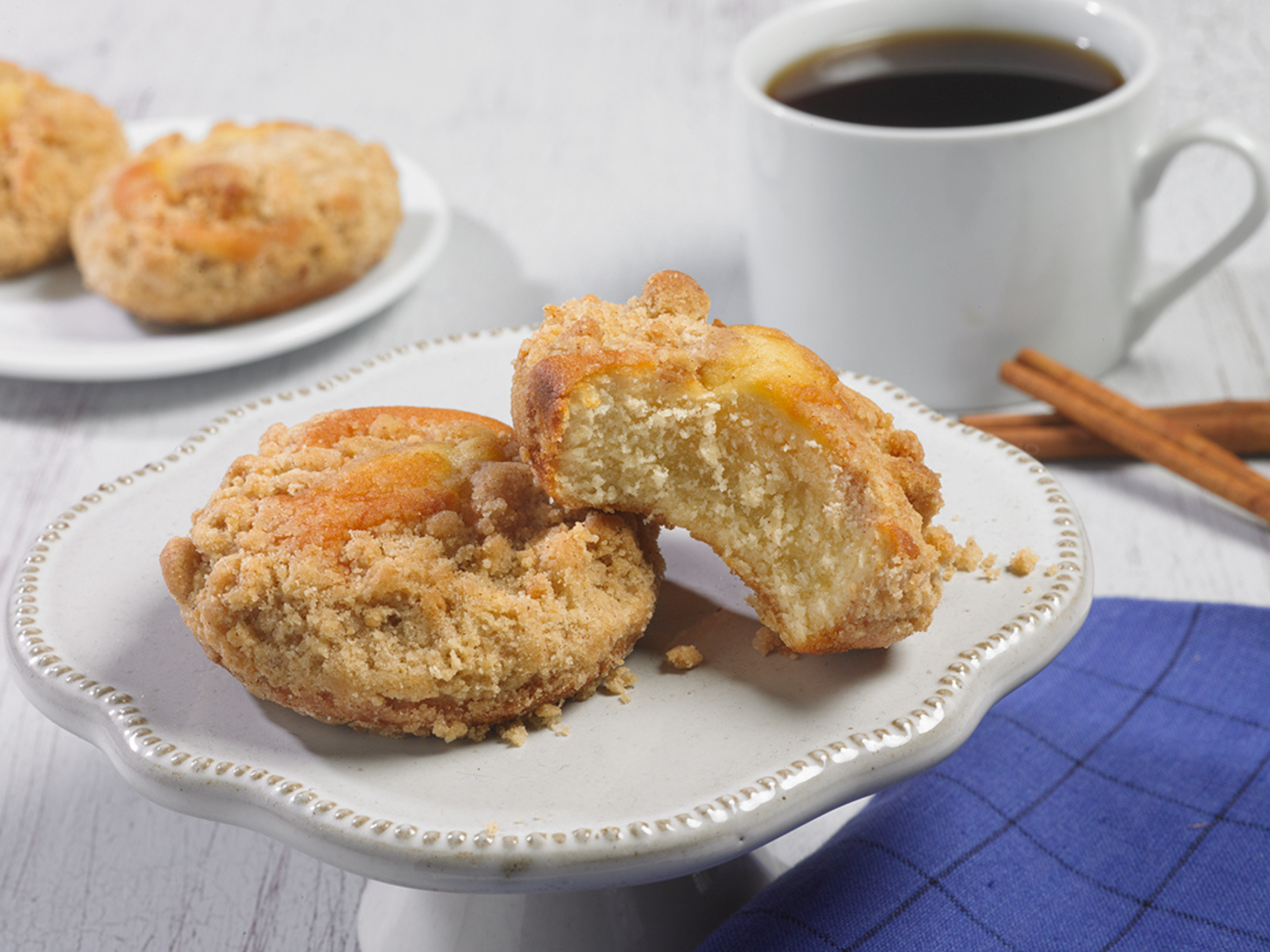 Two cinnamon strudel cakes on a white plate next to a cup of coffee