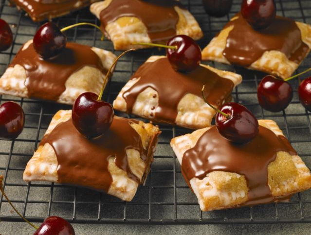 Chocolate covered pastries with cherries on top on a cooling rack