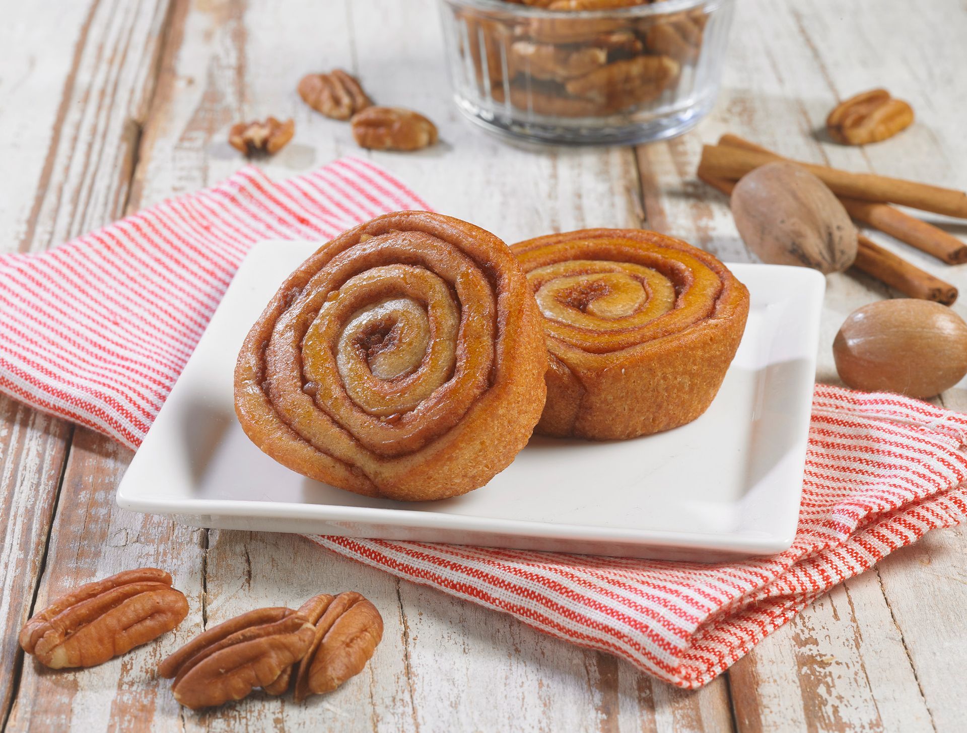 A white plate topped with two cinnamon rolls and pecans
