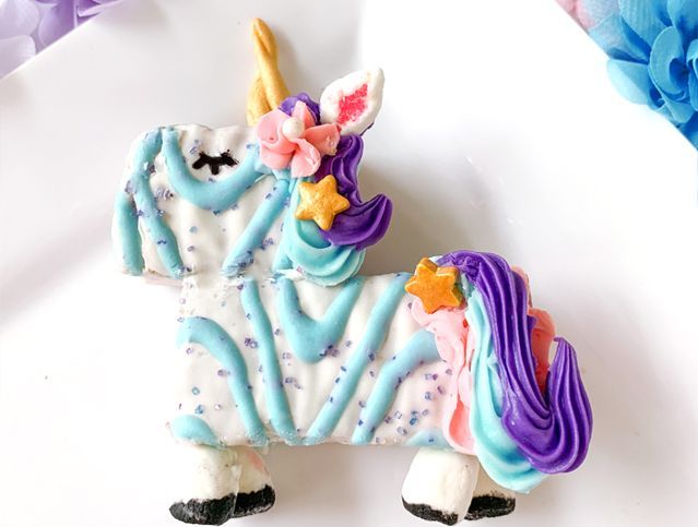 A white plate topped with a cookie in the shape of a unicorn.