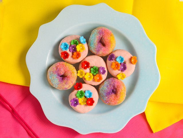 A blue plate topped with pink donuts decorated with flowers and sprinkles