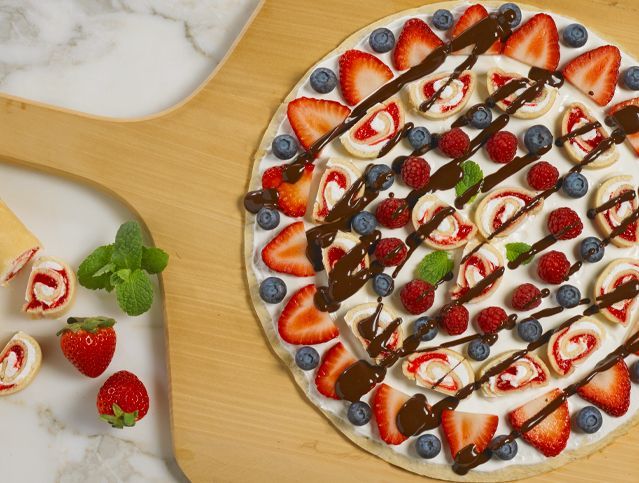 A pizza with strawberries , blueberries and chocolate sauce on it