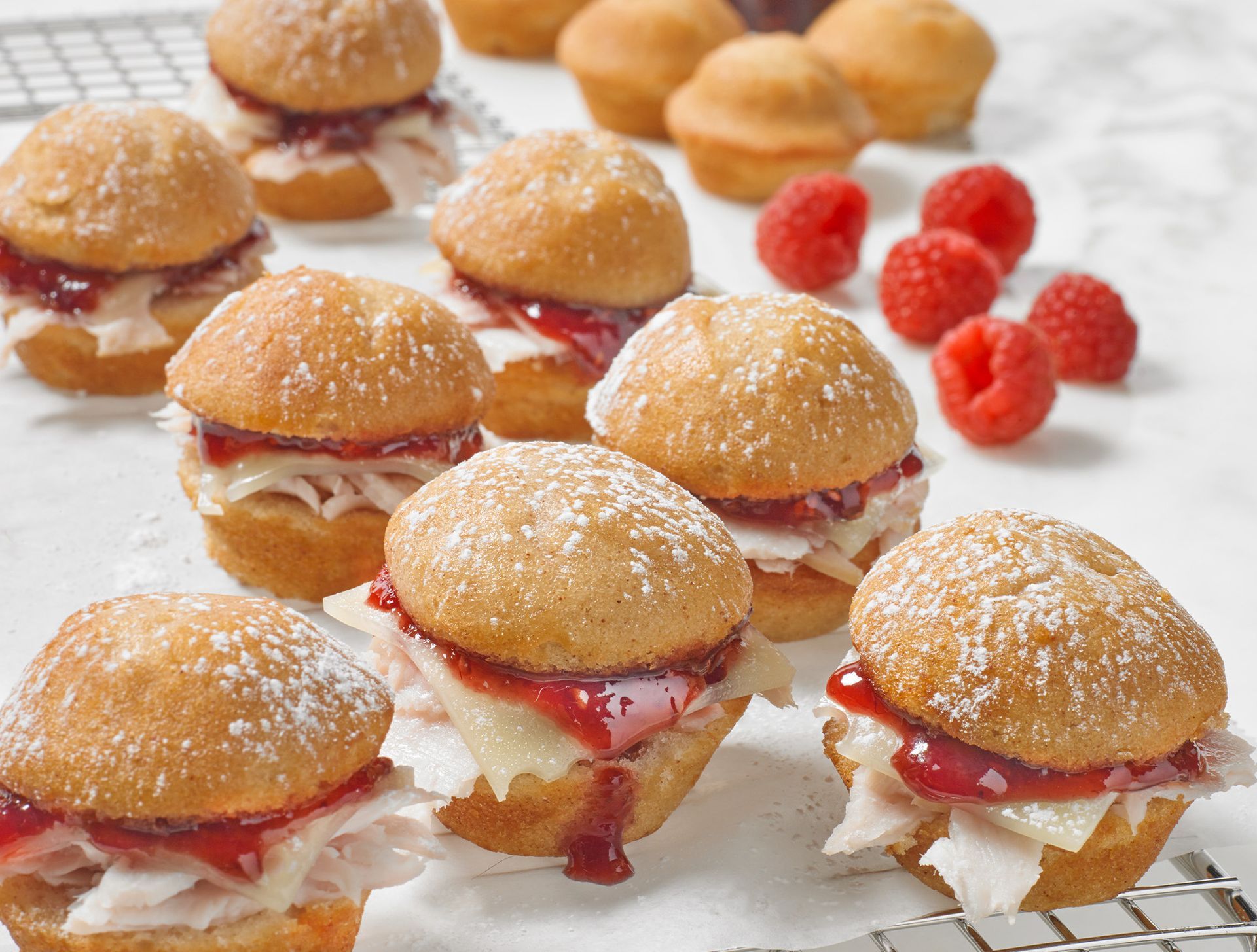 A bunch of mini hamburgers with raspberries in the background