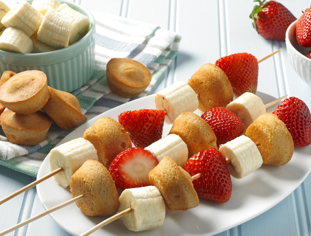 A white plate topped with bananas and strawberries on skewers