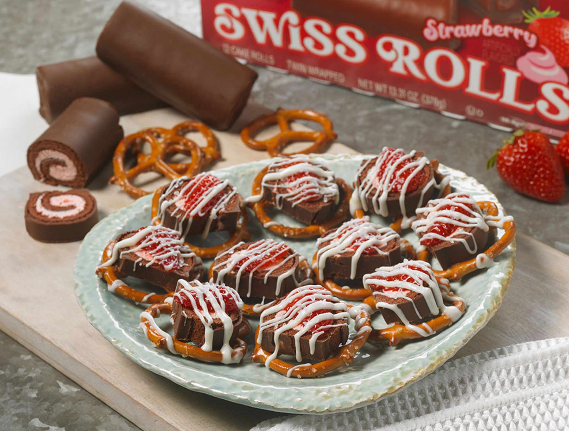 A plate of swiss rolls with strawberries and pretzels