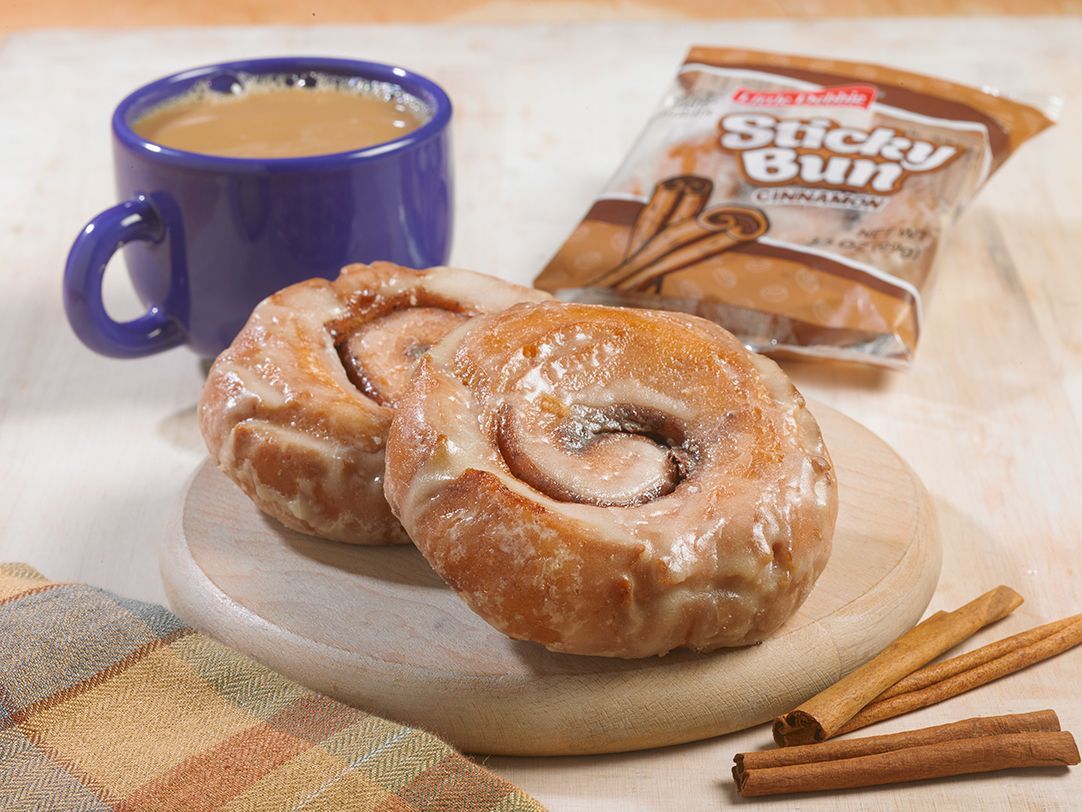 Two cinnamon rolls on a cutting board next to a bag of sticky buns