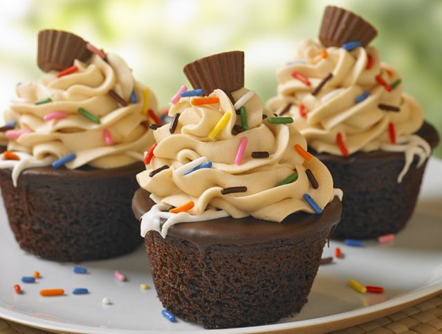 Three chocolate cupcakes with peanut butter frosting and sprinkles on a white plate
