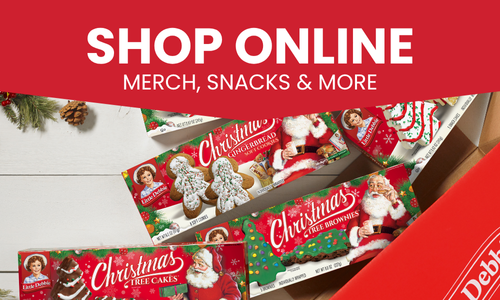 A mug with a picture of cookies on it is on a table next to a plate of food. Text is 