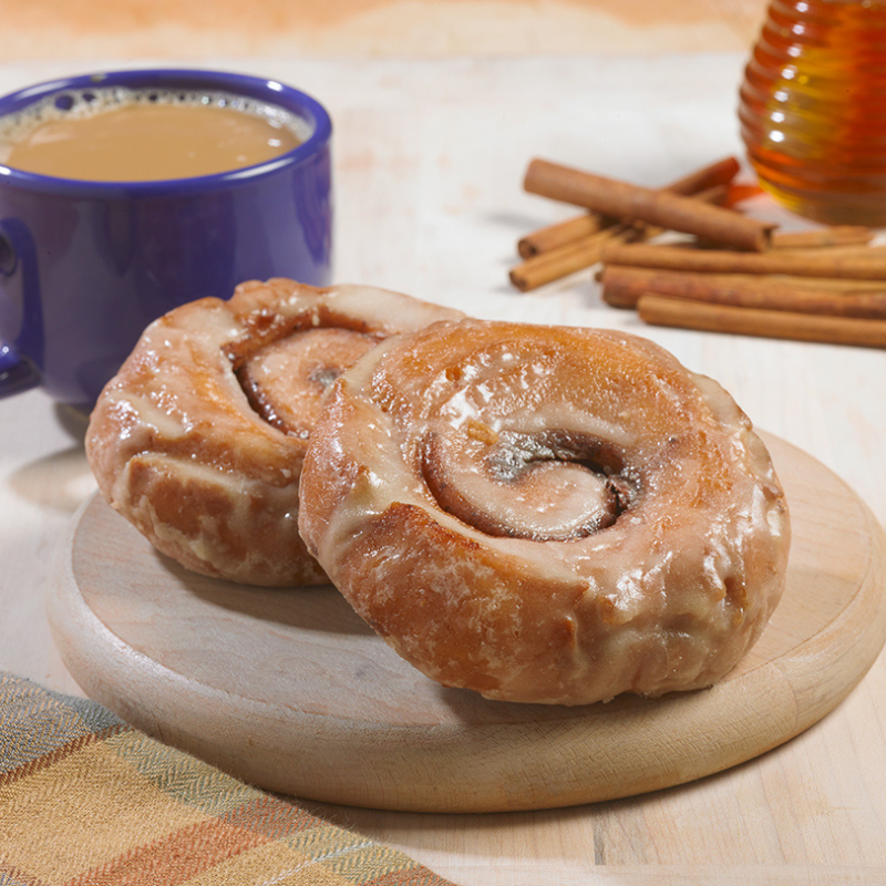 Two cinnamon rolls on a wooden cutting board next to a cup of coffee