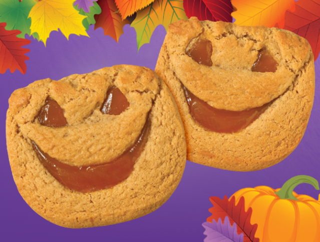 Two cookies with faces carved into them and a pumpkin in the background