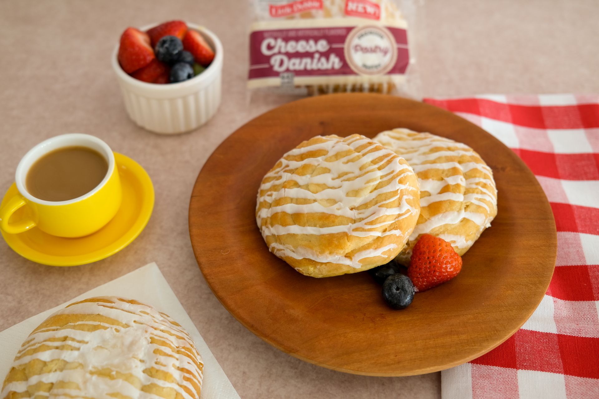 two cheese danish pastries on a wooden plate next two fresh fruit and a package of cheese danish