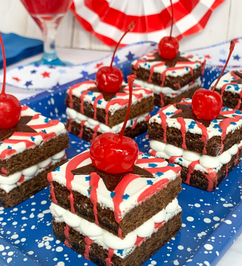 Close-up of festive brownie bites topped with whipped cream and cherries, arranged on a blue speckle