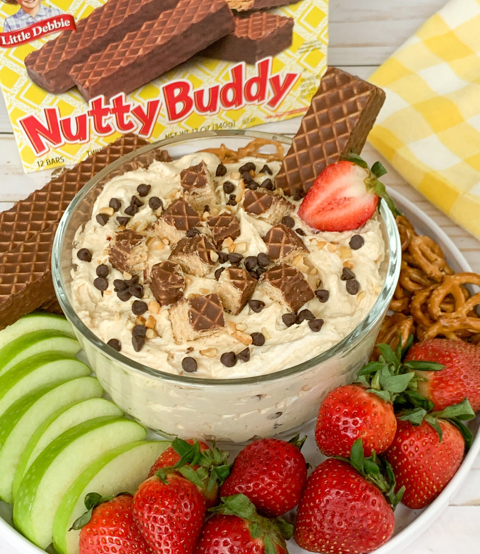 Bowl of Nutty Buddy cheesecake dip served on a platter with fresh fruit and pretzels, with a box of 