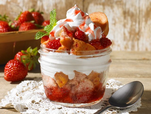 A mason jar filled with strawberries and whipped cream next to a spoon.