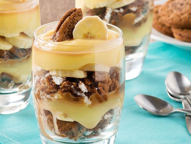 A close up of a dessert in a glass with bananas and cookies on top.