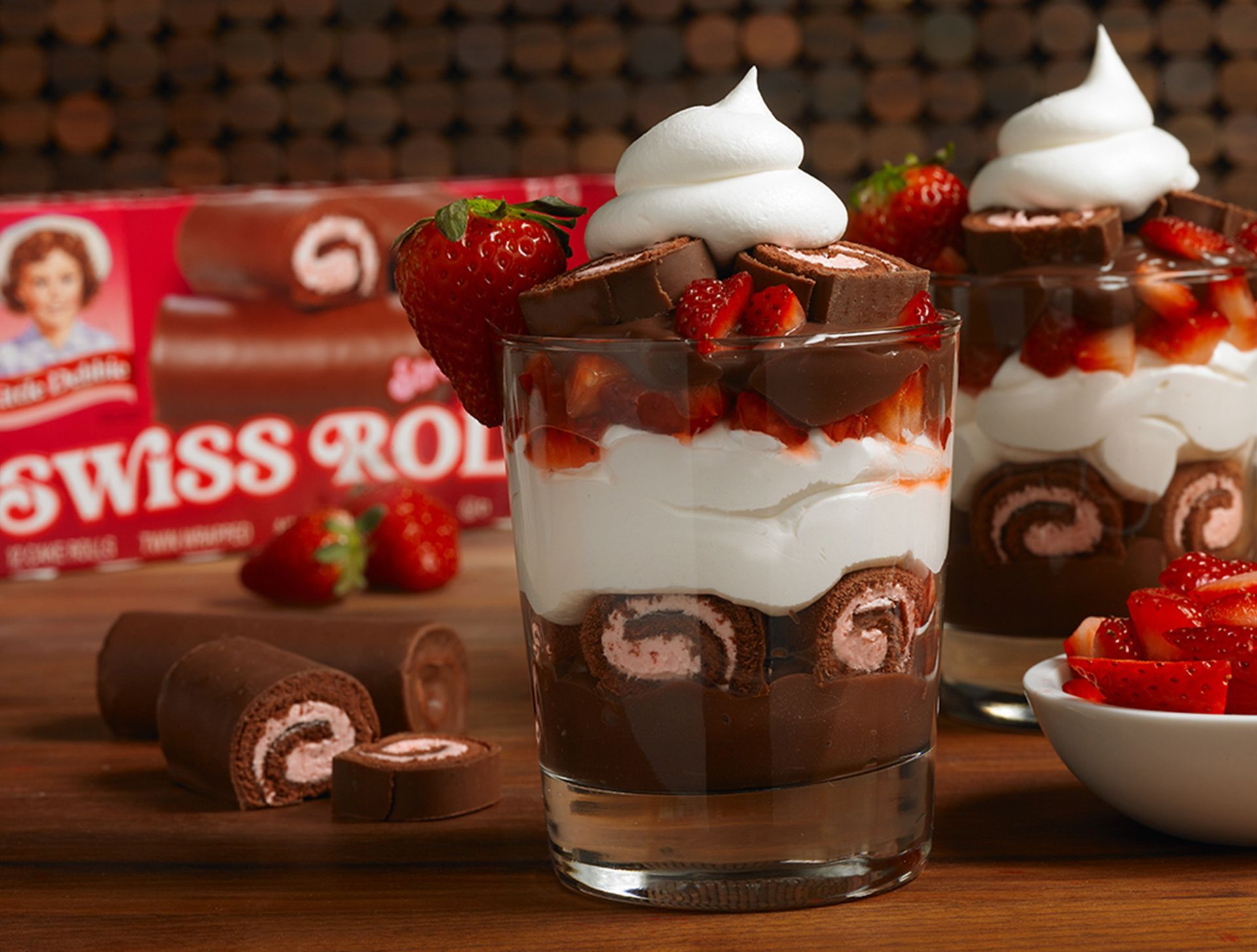 Two glasses of swiss roll dessert with strawberries and whipped cream