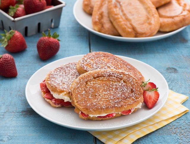 Two french toast sandwiches with strawberries and whipped cream on a white plate.