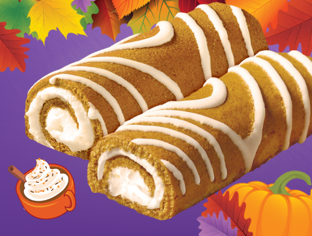 Two pumpkin rolls with white frosting and a slice of pumpkin pie in the background