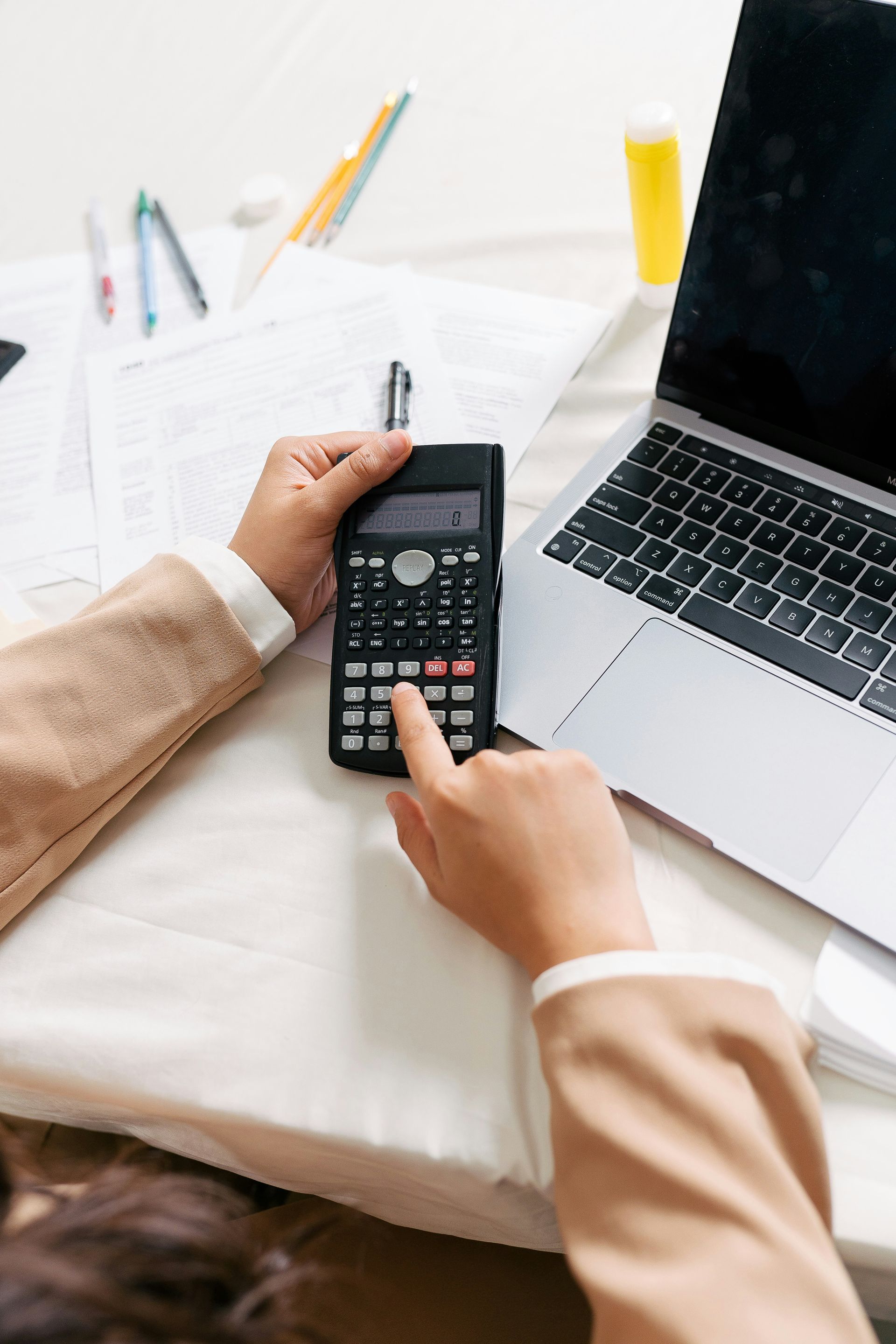Person using a calculator at a desk with a laptop and papers.