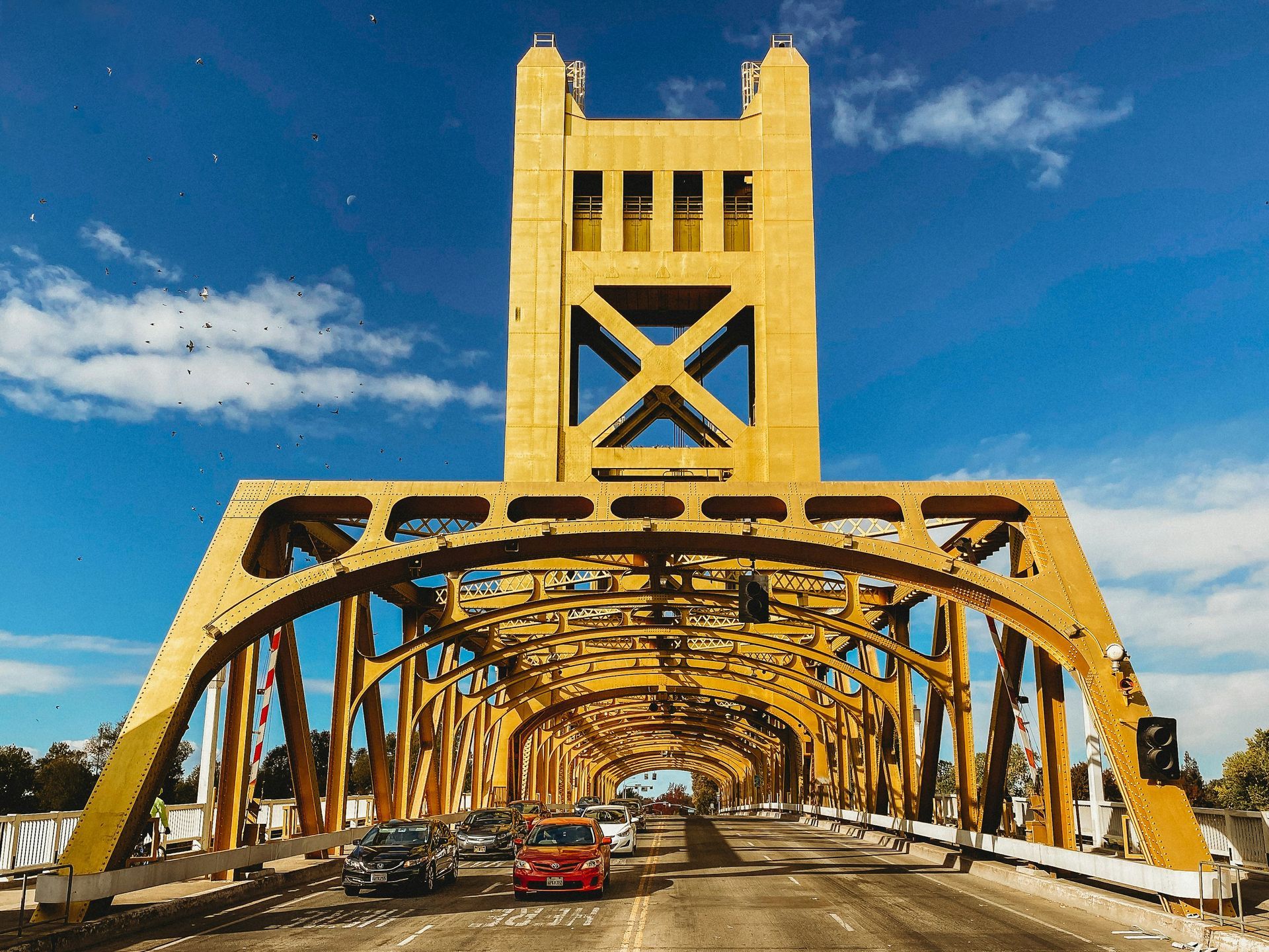 Yellow Tower Bridge over roadway with cars on a sunny day.