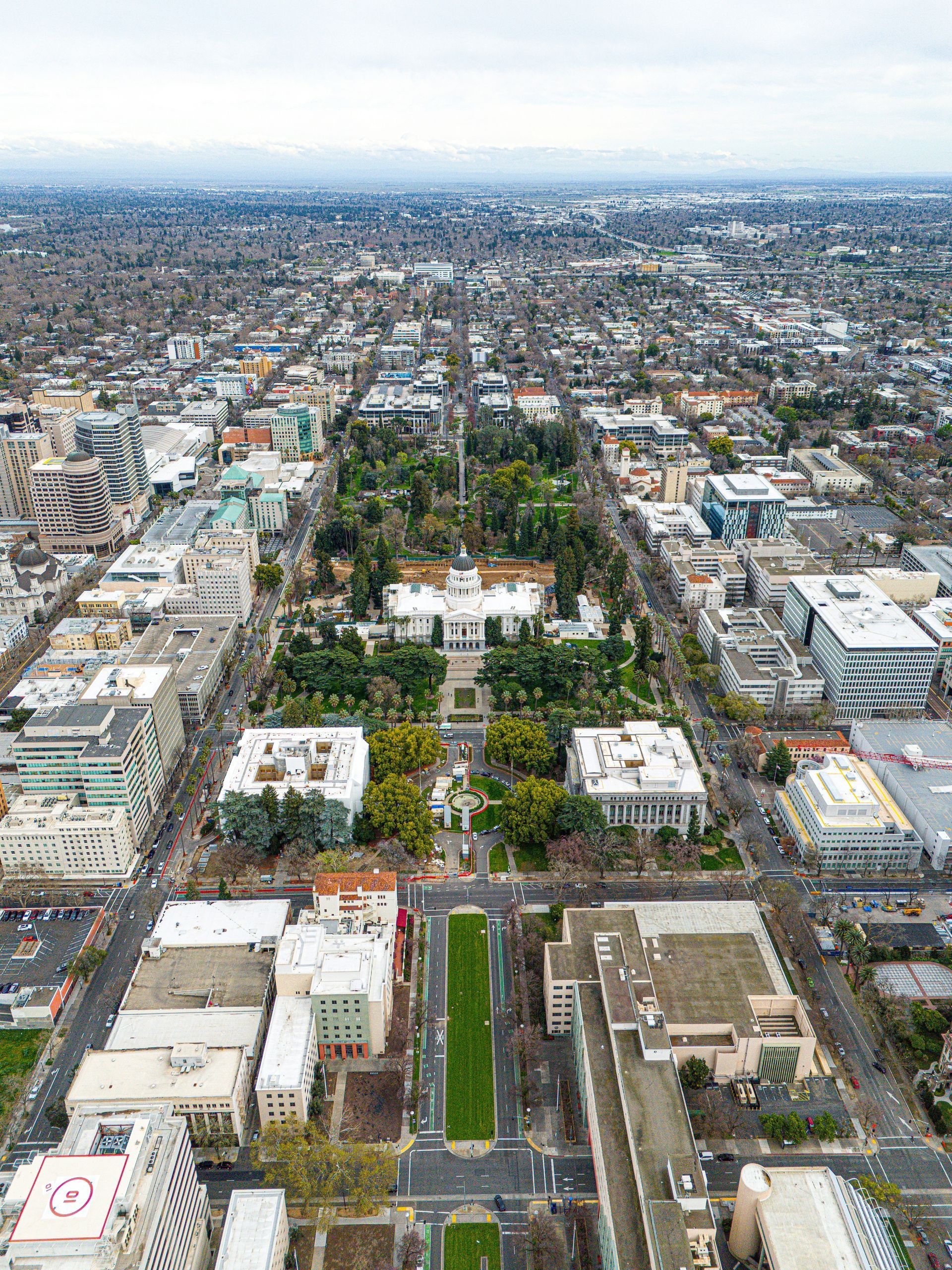 Aerial view of a city with a large green park and the white California State Capitol building.