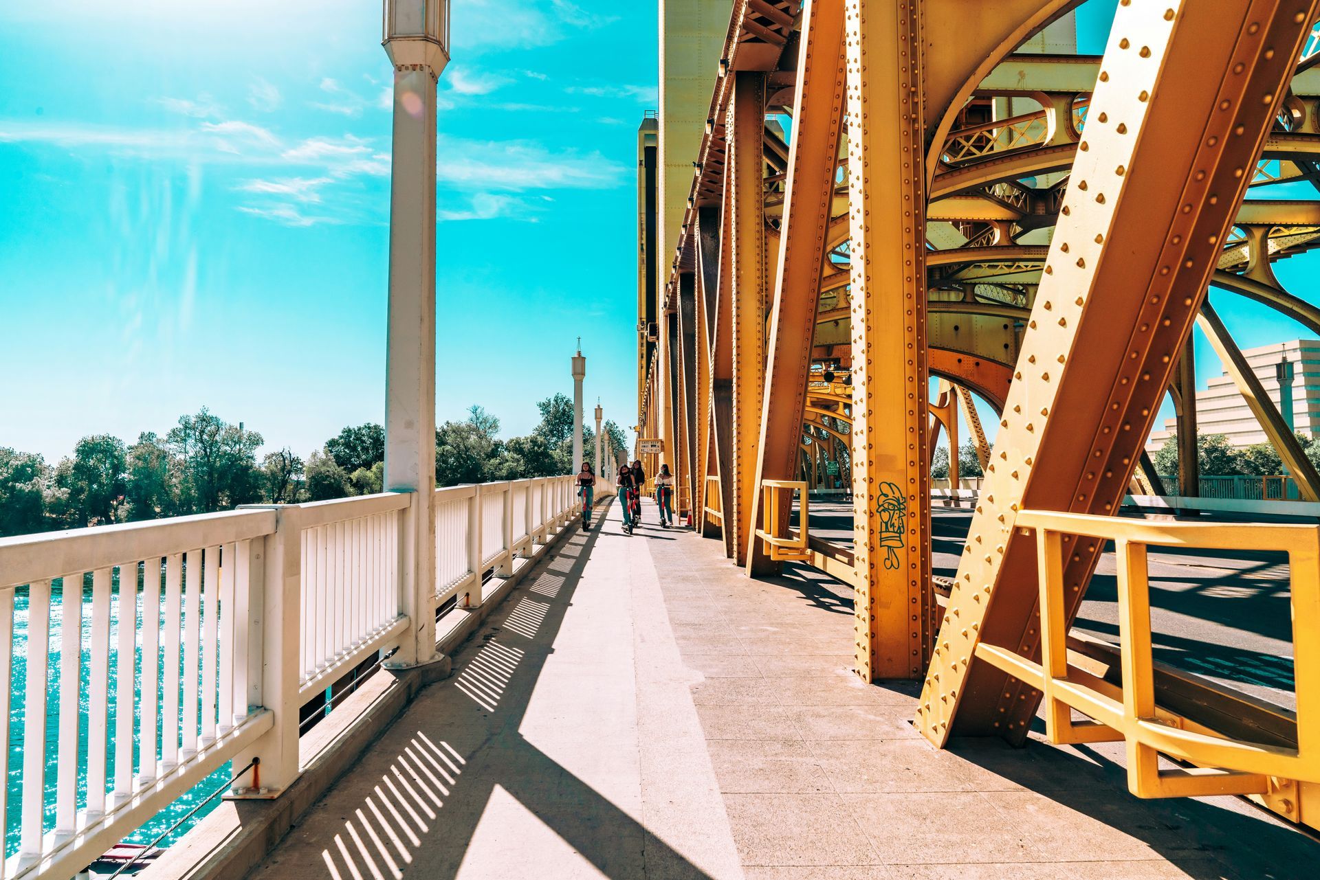 Yellow bridge with a walkway, blue sky, and two people walking.