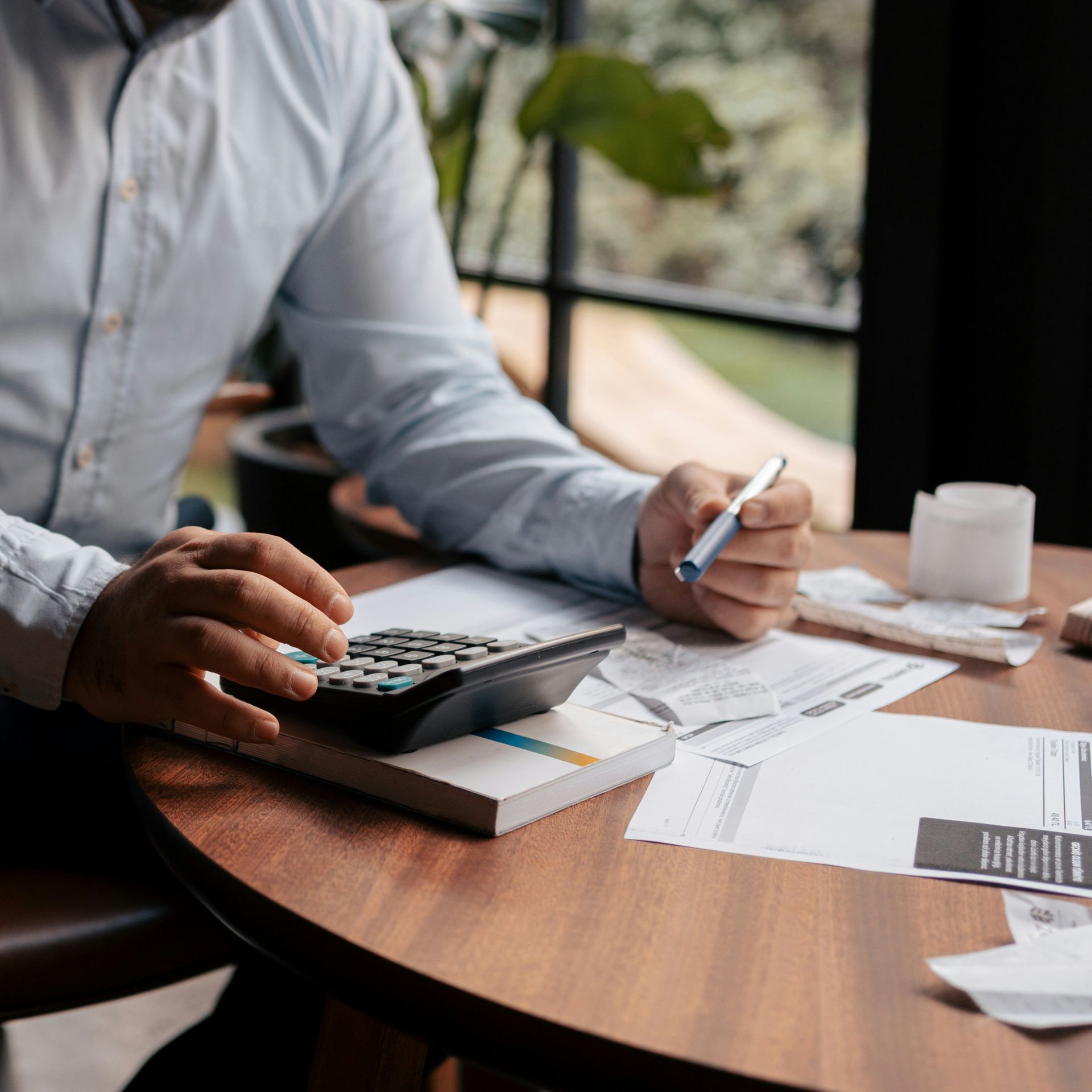 Person using a calculator, holding a pen, reviewing documents at a table.