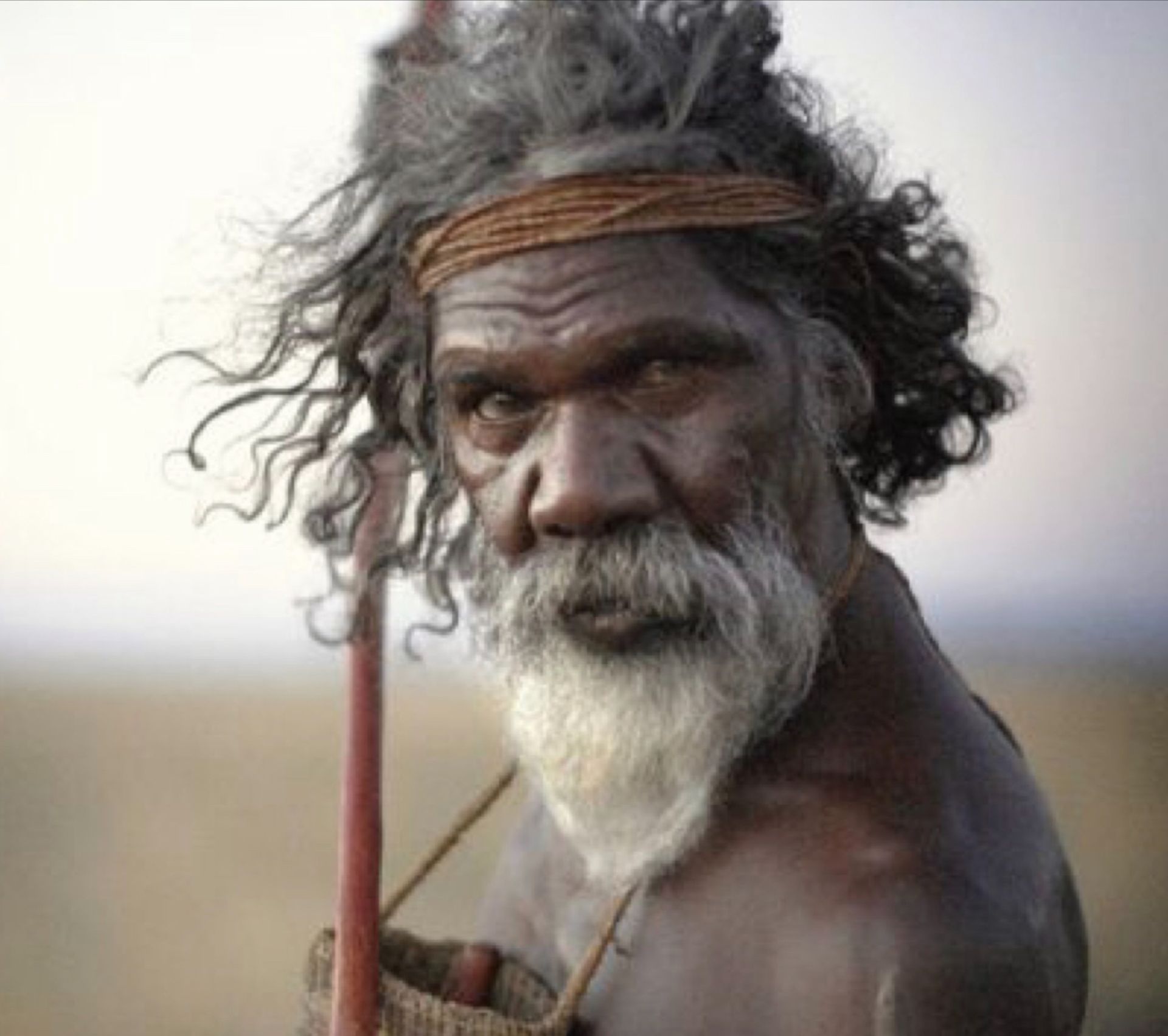 A man with a beard and a headband is holding a stick.