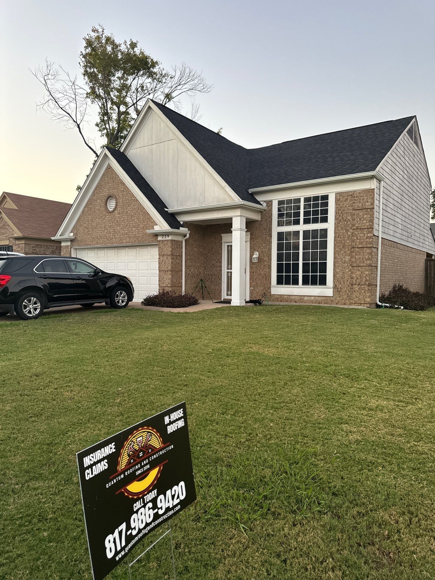 A house with a black car parked in front of it and a sign in front of it.