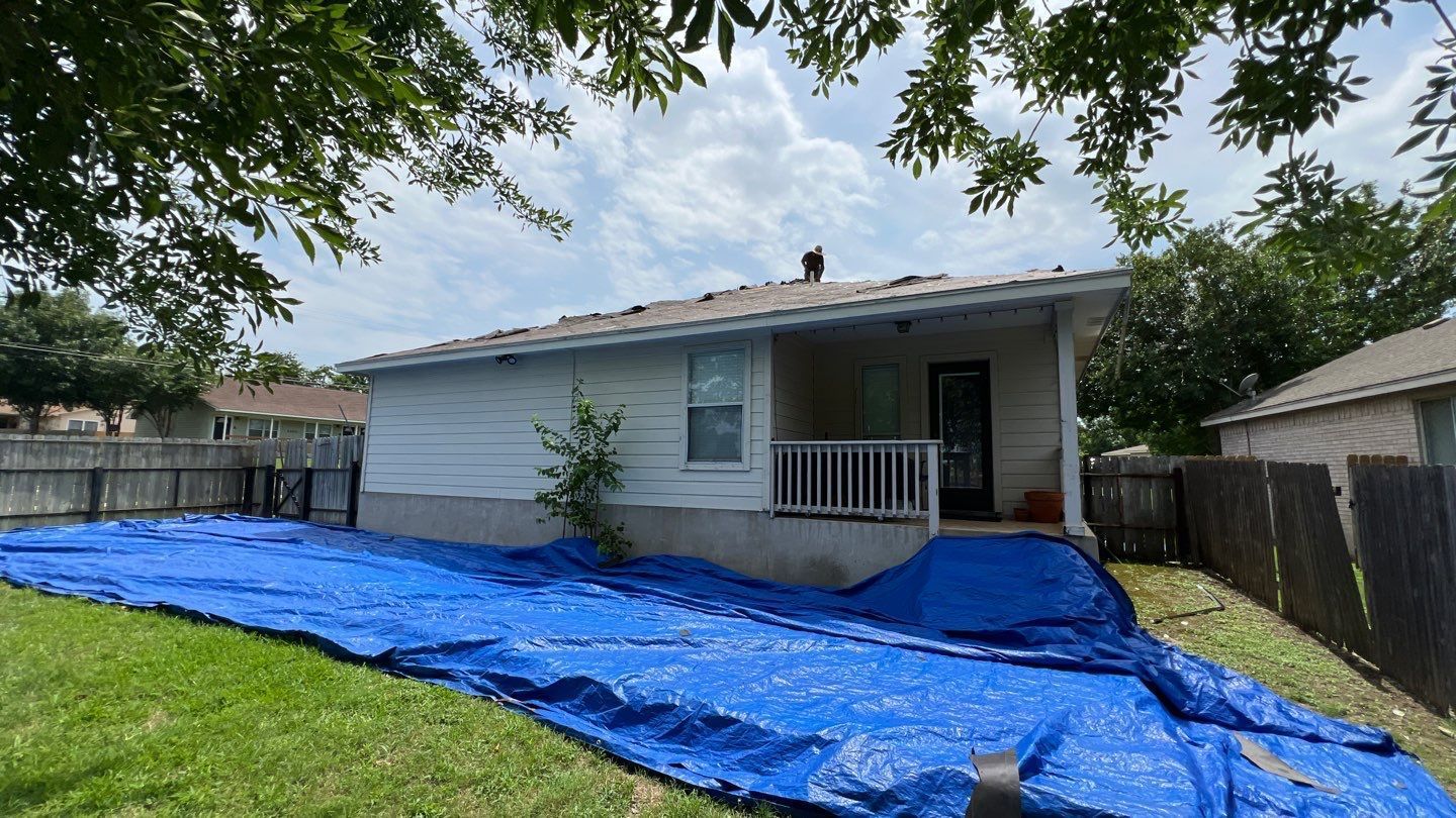 A house with a blue tarp on the ground in front of it.