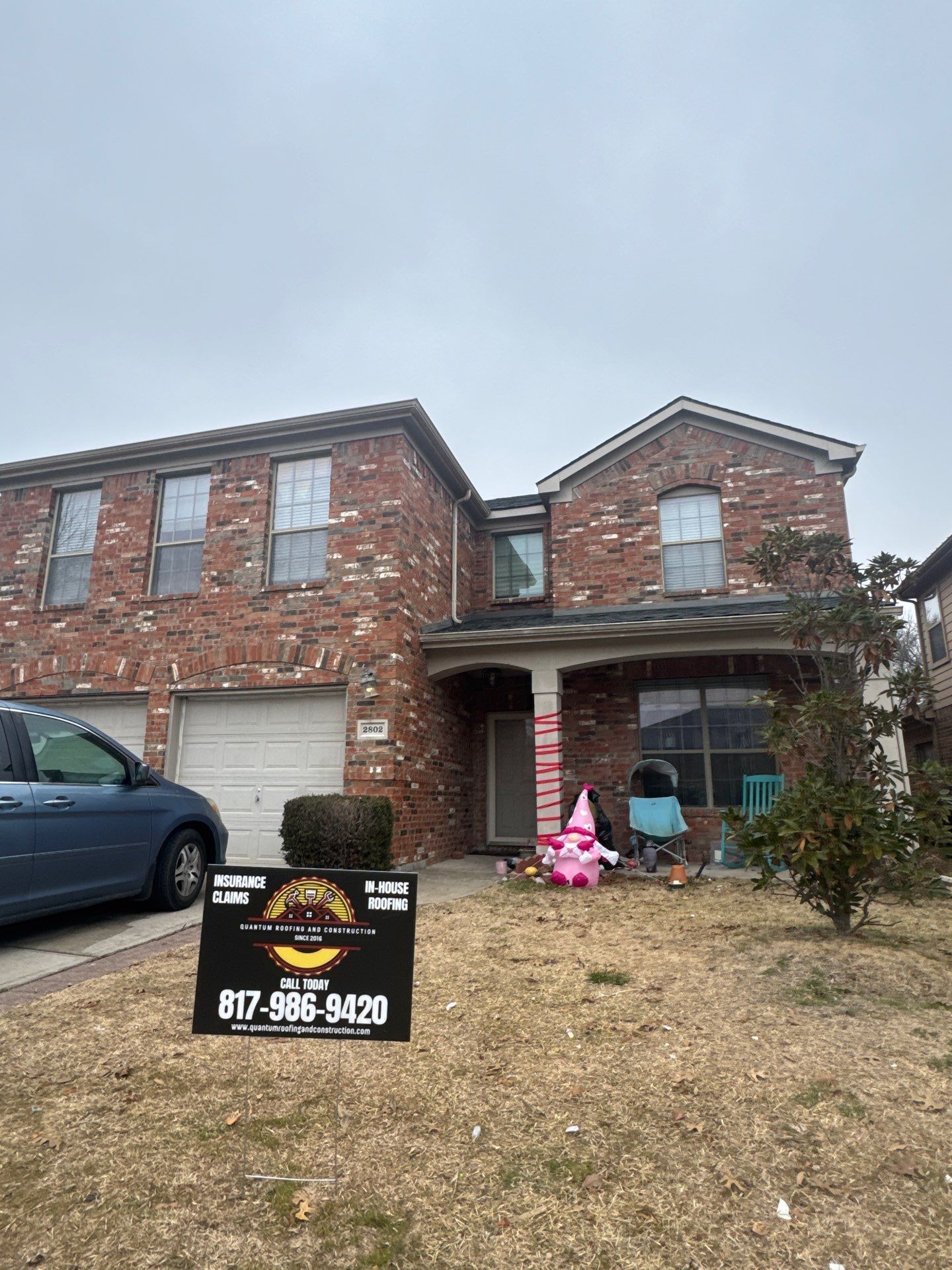 A brick house with a sign in front of it and a car parked in front of it.