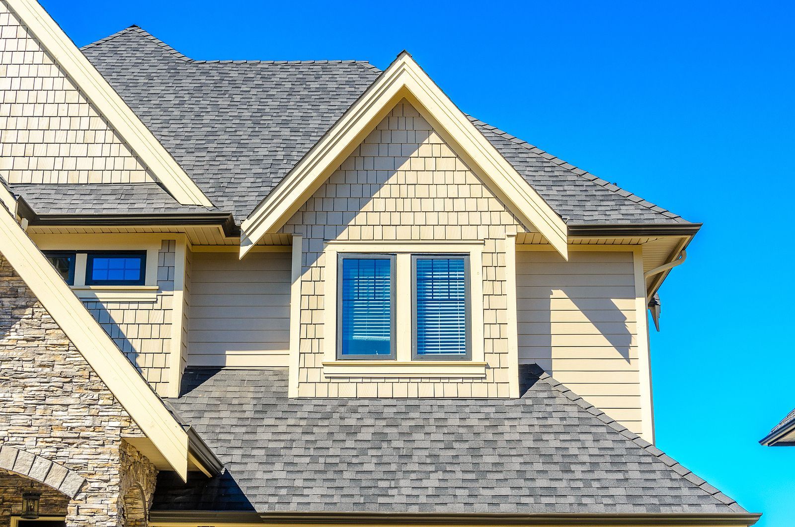 House with gray shingle roof, beige siding, small gable window, and blue sky backdrop.