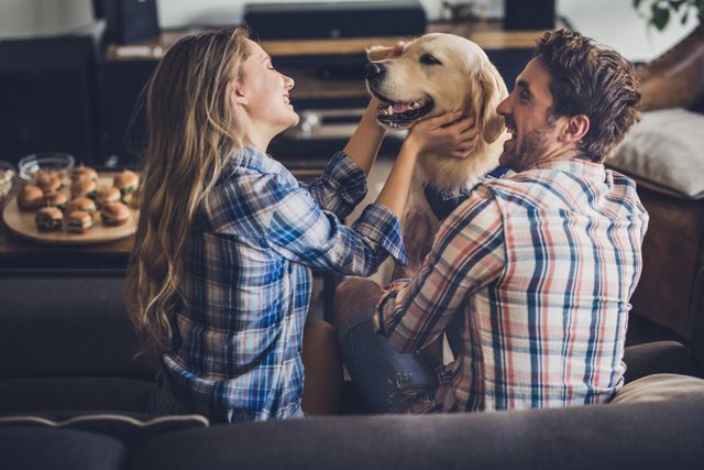 man and woman cuddling dog on couch