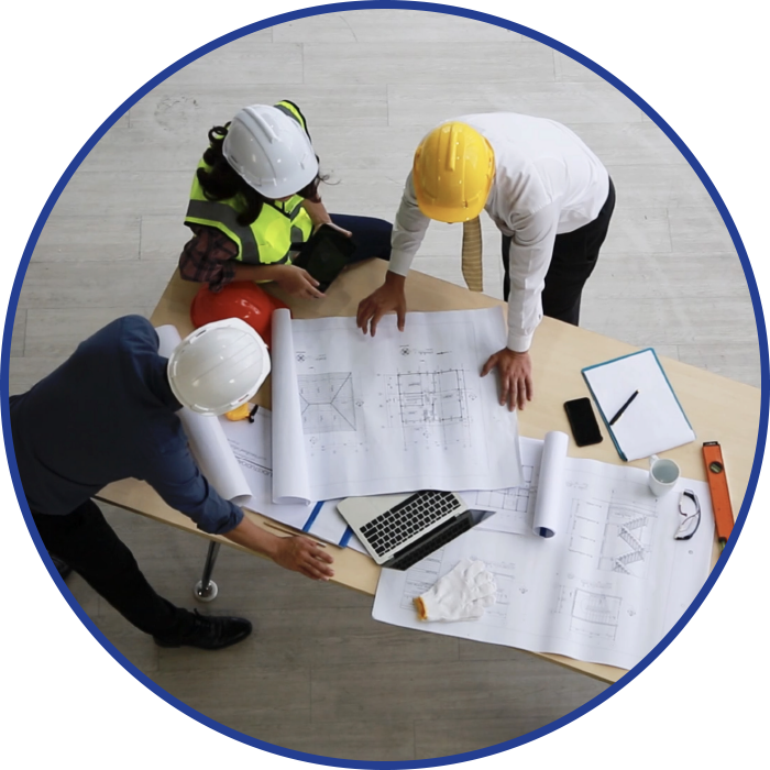 Construction workers, in hard hats, review blueprints at a table, discussing a project.
