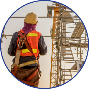 Construction worker in safety gear on a scaffold, looking up at a crane, wearing a hard hat and safety vest.