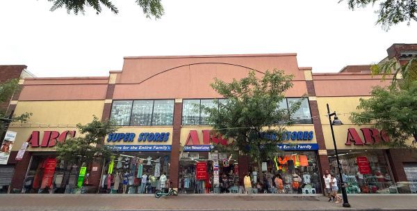 Exterior view of ABC Super Store; building with large windows, clothing on display, people walking in front.