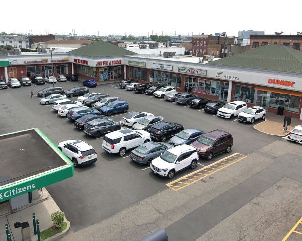 A shopping center with cars parked in front of storefronts on a sunny day.