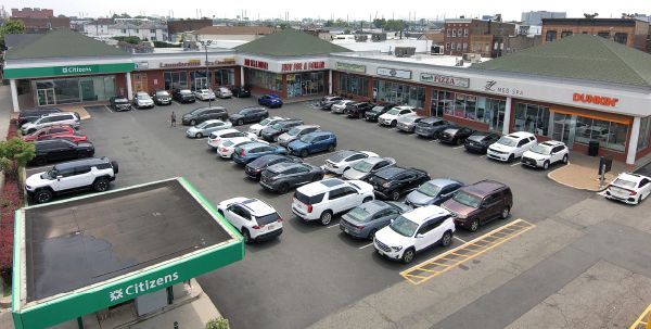 A shopping center with cars parked in front of storefronts on a sunny day.
