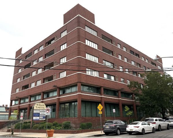 Brick building with multiple floors, street parking and road signs in front.