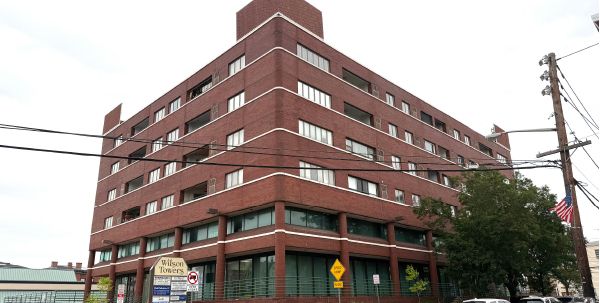 Brick building with multiple floors, street parking and road signs in front.