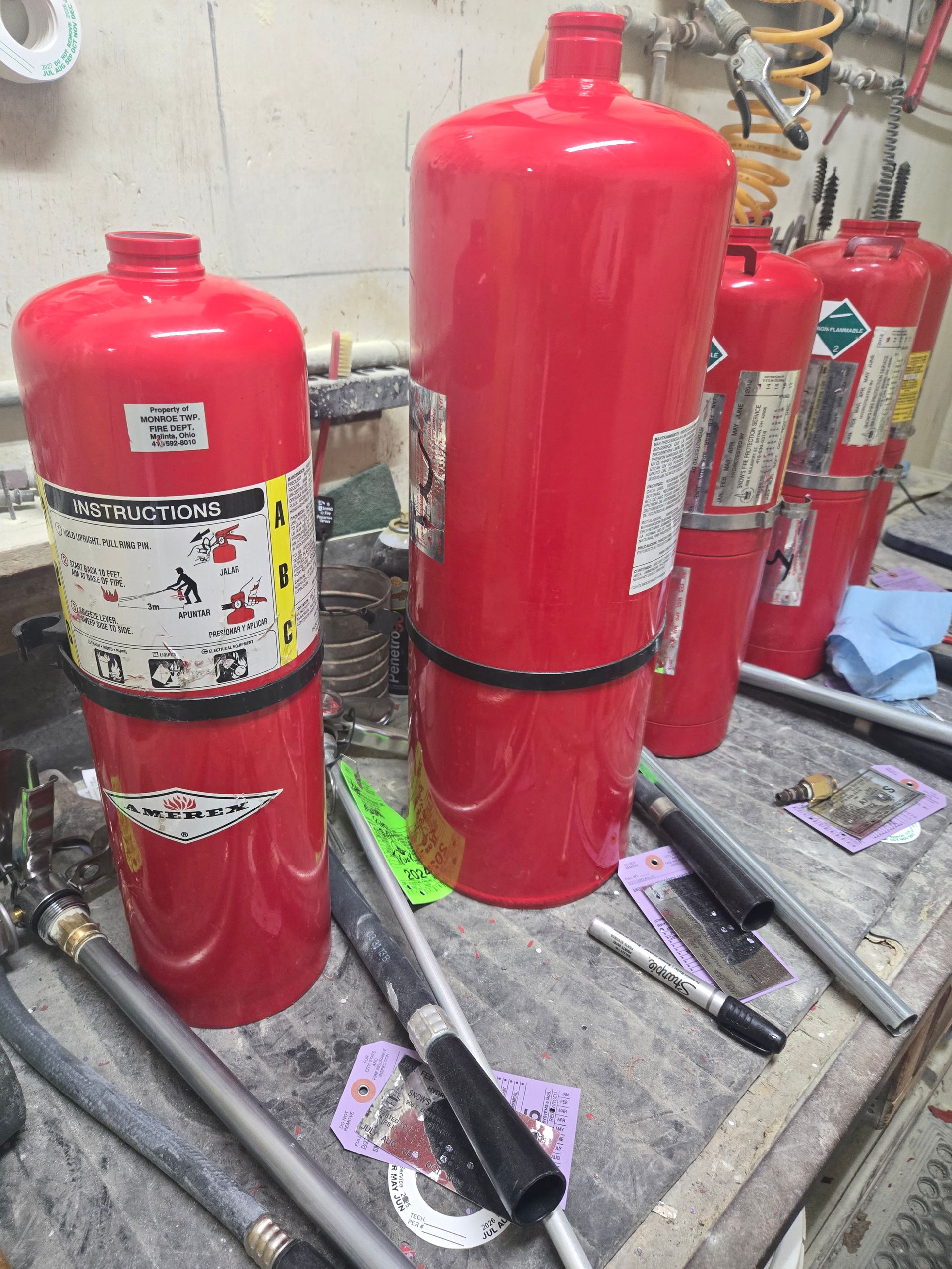 Red fire extinguishers on a workbench. Some have labels, and are ready for use.
