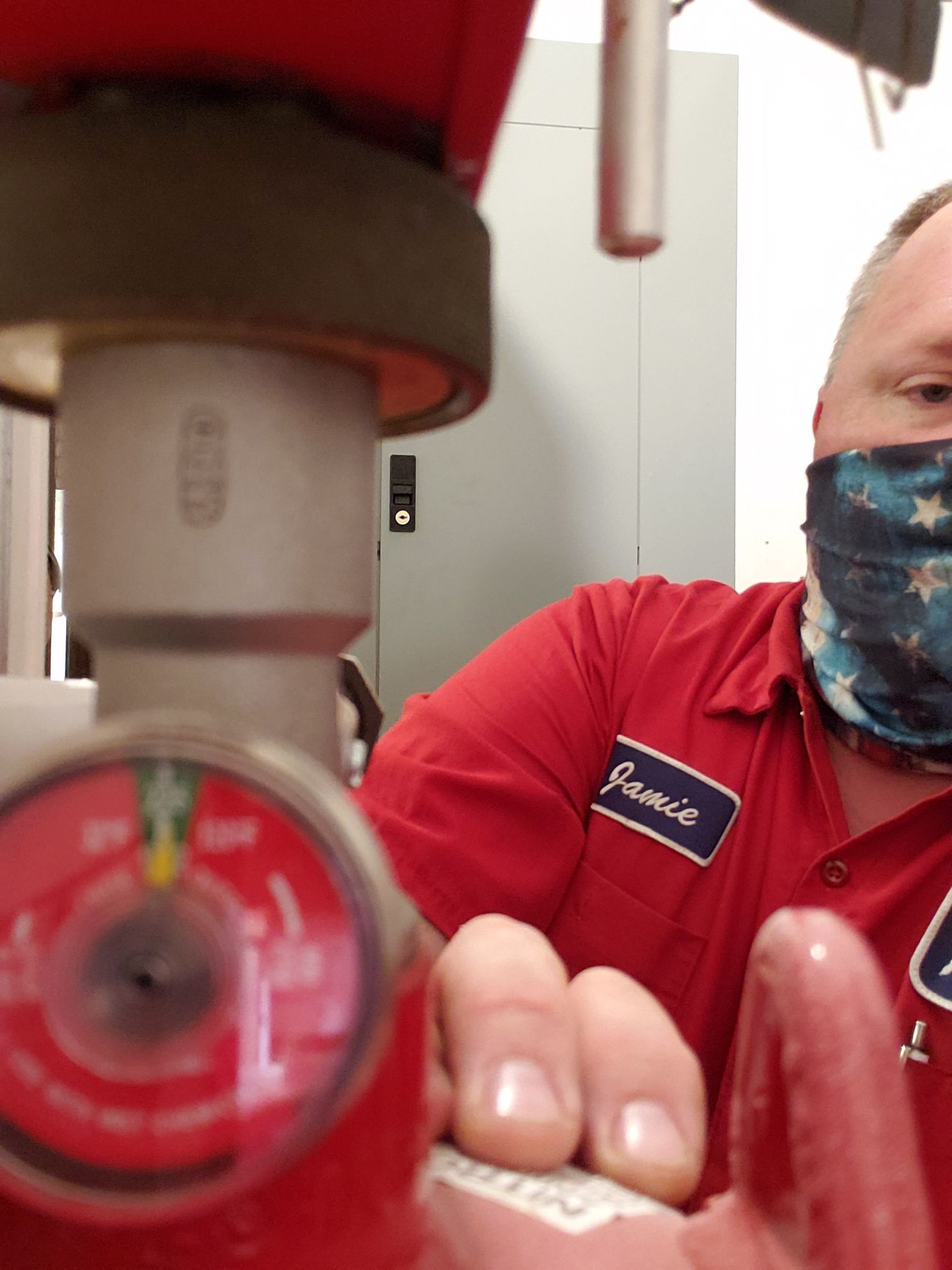 Man in red shirt and mask adjusts a red gauge on equipment.