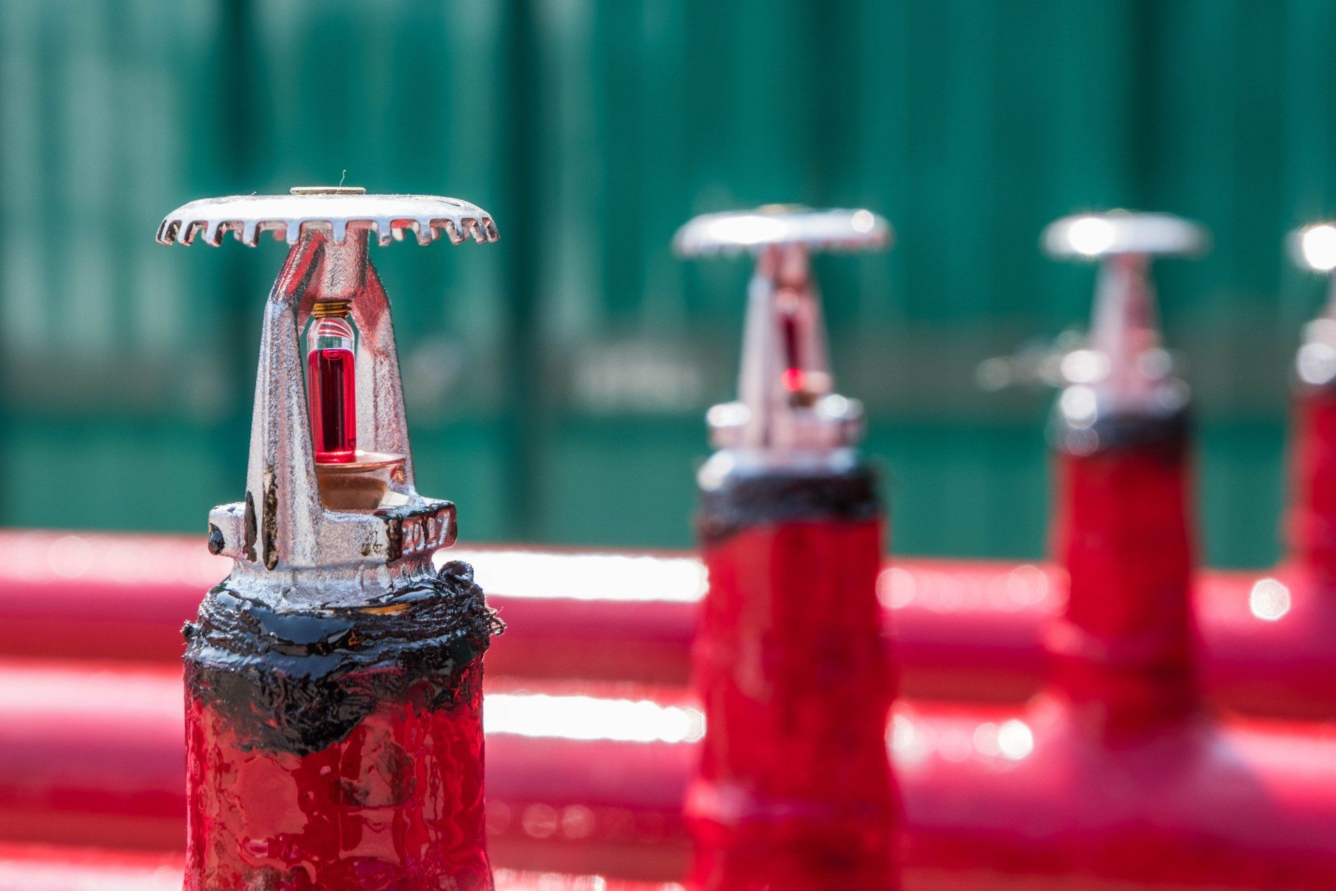 Fire sprinklers mounted on red pipes, against a green wall.