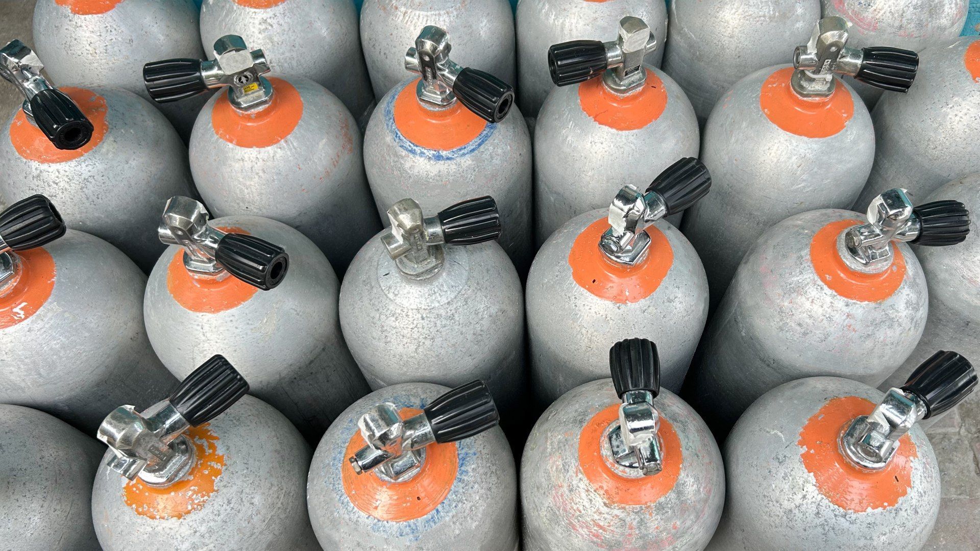 Rows of silver scuba tanks with orange collars and black valves.