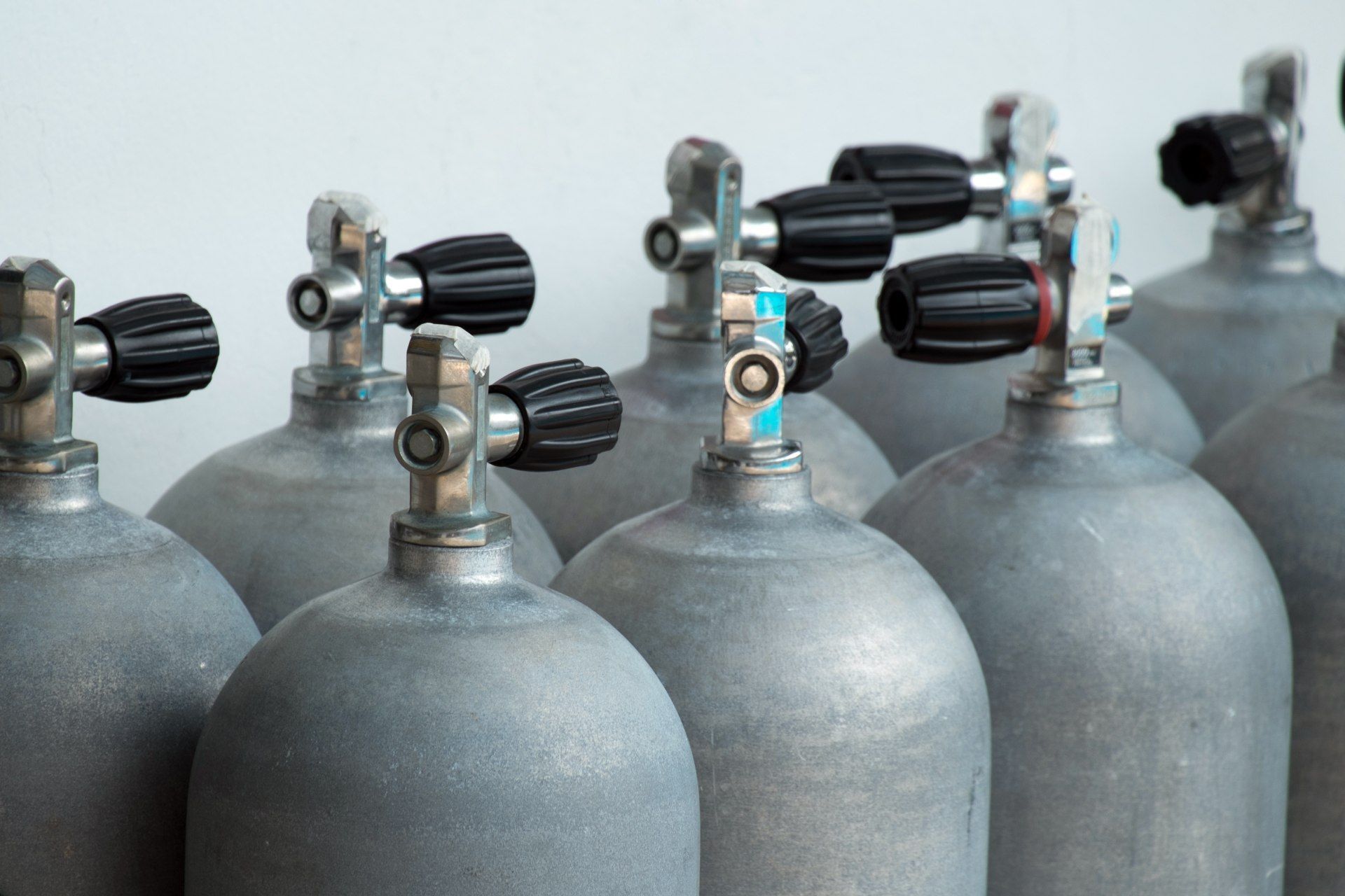 Silver oxygen tanks with black knobs, lined up in a row.