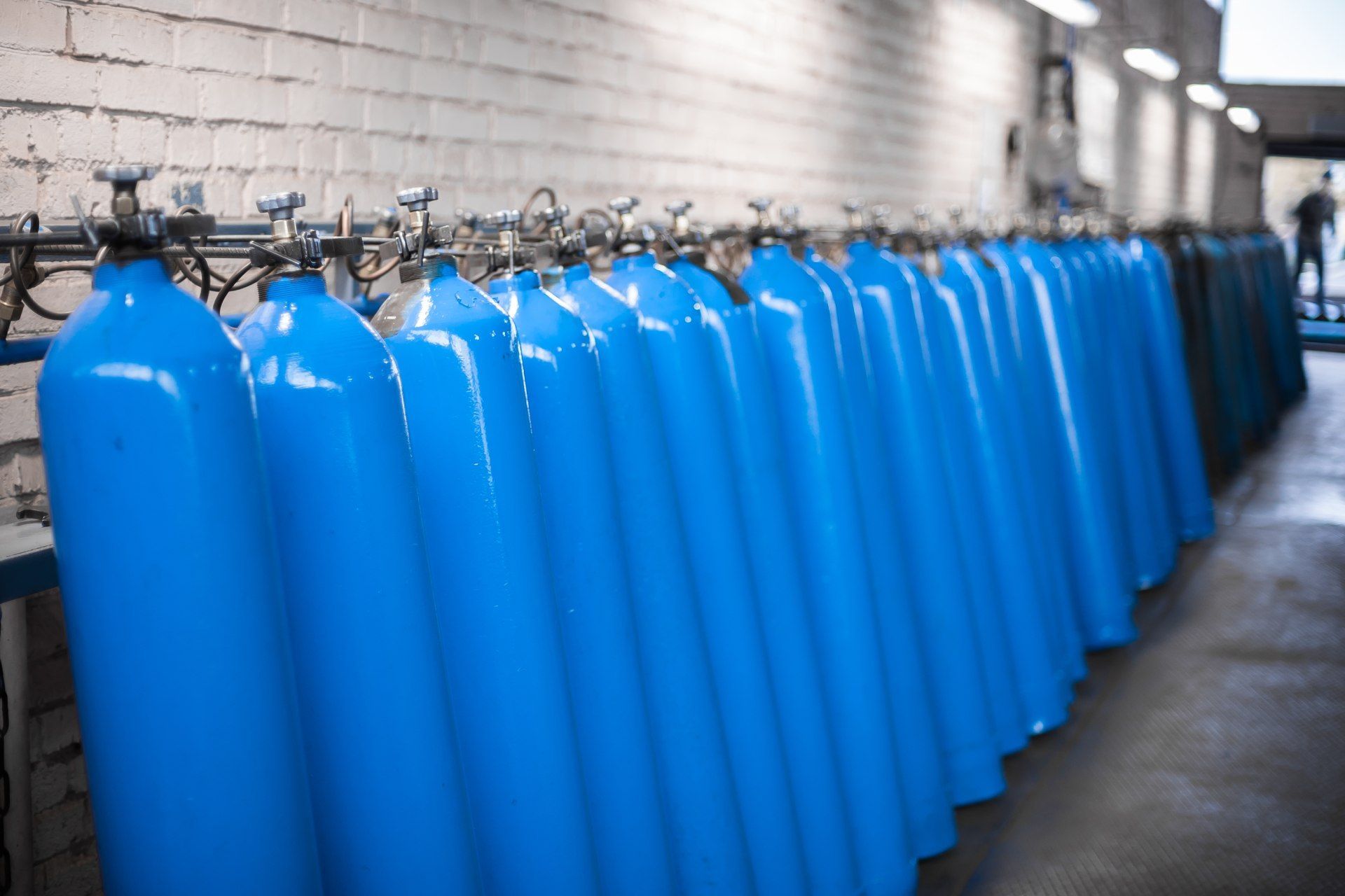 Blue oxygen tanks in a row against a brick wall.