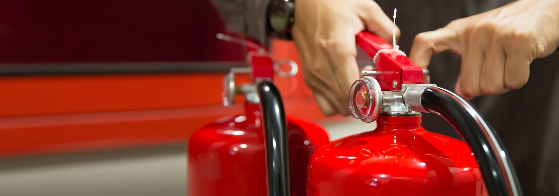 Person inspecting a red fire extinguisher, checking the pressure gauge and pin.