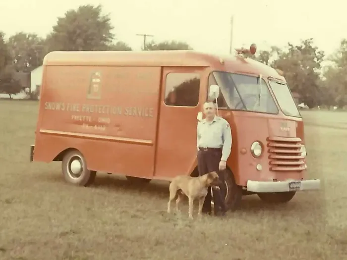 Man stands with dog next to a red van, 