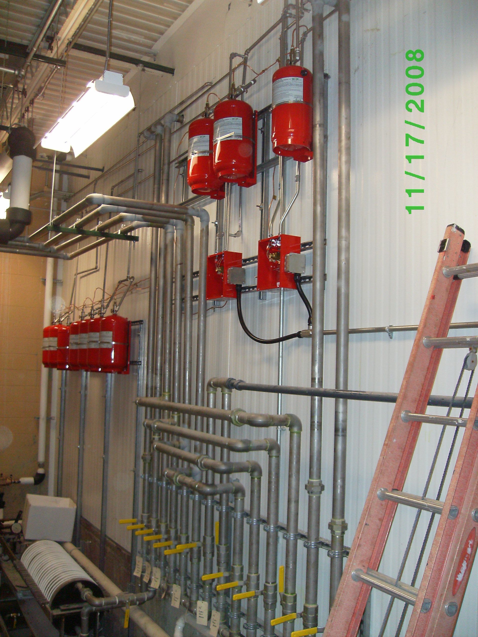 Red fire suppression system with pipes and valves on a wall; red ladder leans on the right.